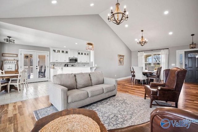 living room featuring a chandelier, high vaulted ceiling, french doors, and light wood finished floors