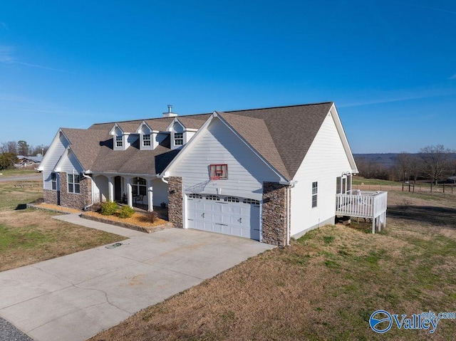 cape cod home with driveway, a garage, stone siding, roof with shingles, and a front lawn