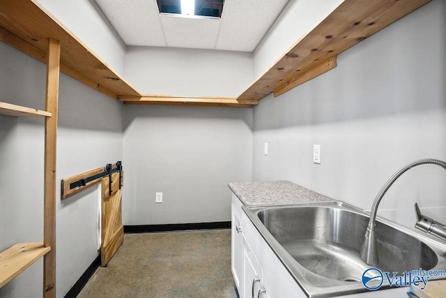 kitchen with baseboards, white cabinets, light countertops, a paneled ceiling, and a sink