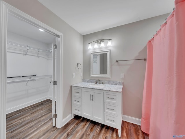 bathroom with baseboards, wood finished floors, a spacious closet, and vanity