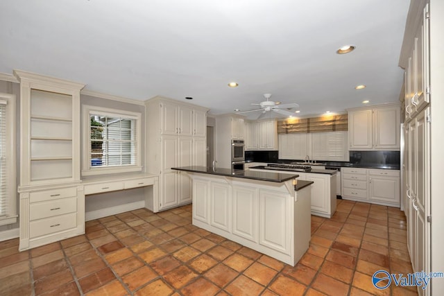 kitchen with recessed lighting, a sink, a kitchen island, built in study area, and dark countertops