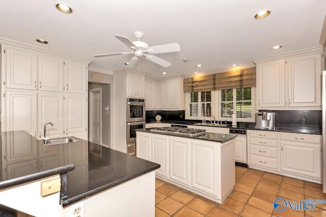 kitchen with dark countertops, appliances with stainless steel finishes, white cabinets, a kitchen island, and a sink