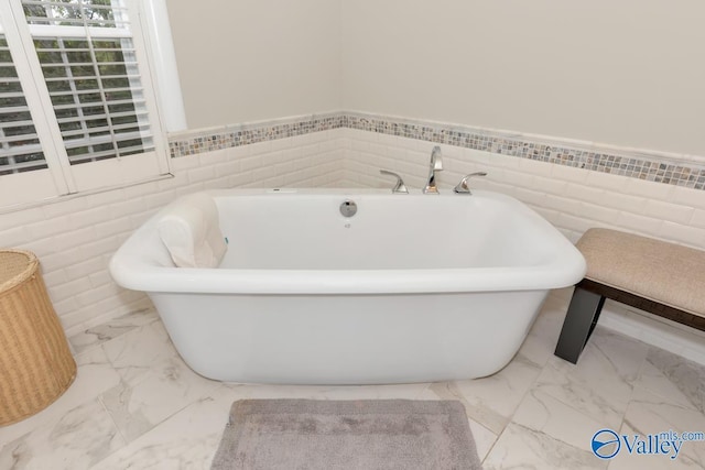 full bath featuring marble finish floor, wainscoting, and a soaking tub