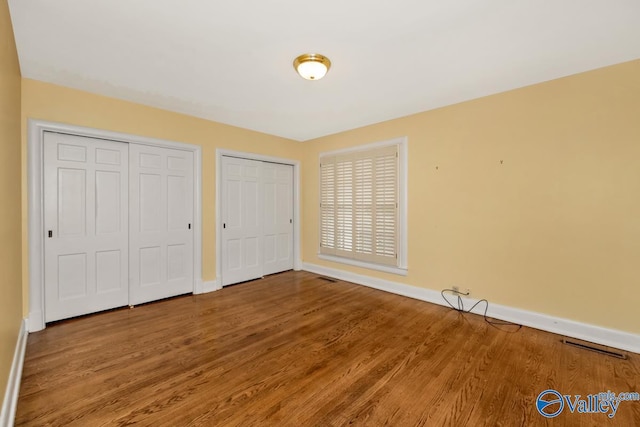 unfurnished bedroom featuring visible vents, baseboards, multiple closets, and wood finished floors