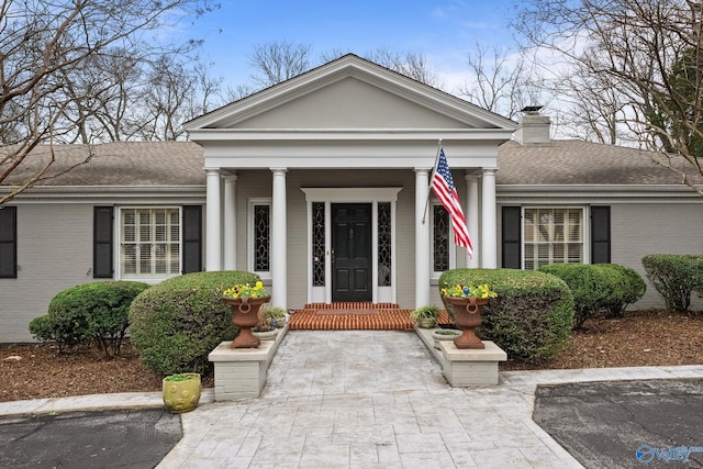 view of front of property featuring brick siding, a chimney, and roof with shingles