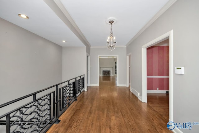 corridor featuring baseboards, wood finished floors, crown molding, a notable chandelier, and recessed lighting