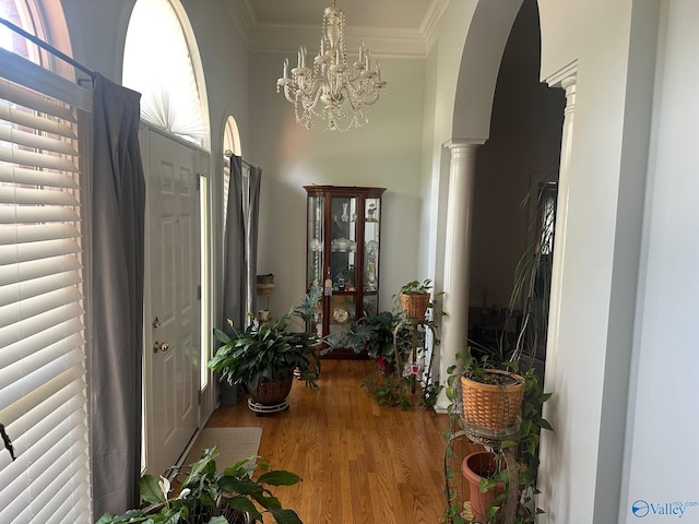 hall with crown molding, wood finished floors, ornate columns, arched walkways, and a notable chandelier