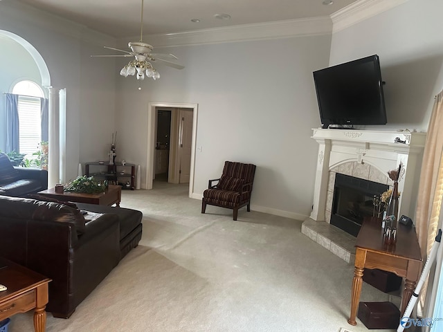 living area with ornamental molding, baseboards, light colored carpet, a tiled fireplace, and a ceiling fan