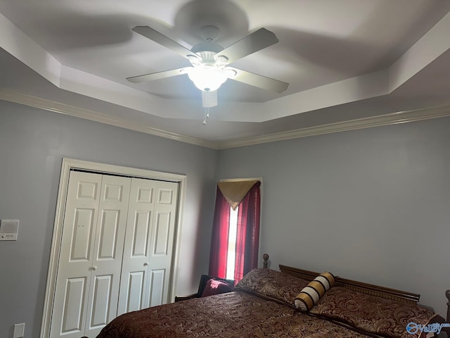 bedroom with a closet, crown molding, a raised ceiling, and ceiling fan