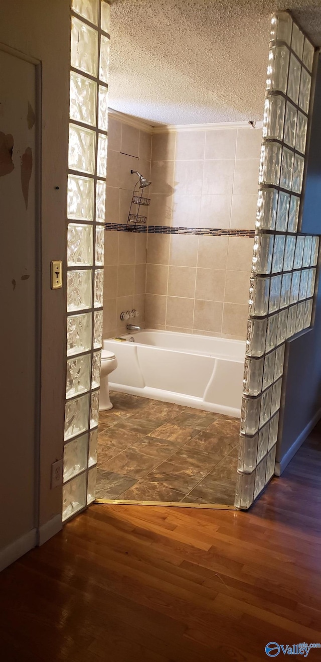 bathroom with toilet, wood-type flooring, a bath, and a textured ceiling