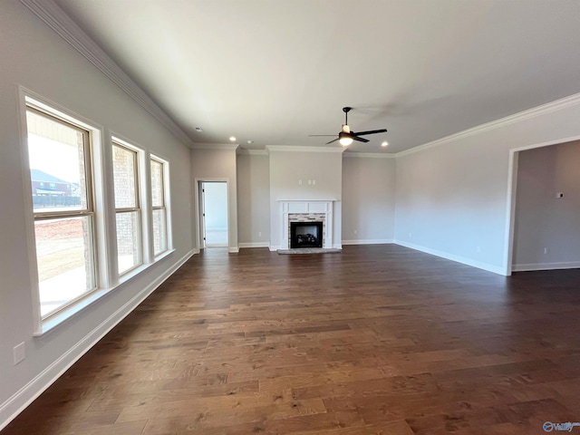 unfurnished living room with dark wood finished floors, crown molding, a fireplace with raised hearth, a ceiling fan, and baseboards