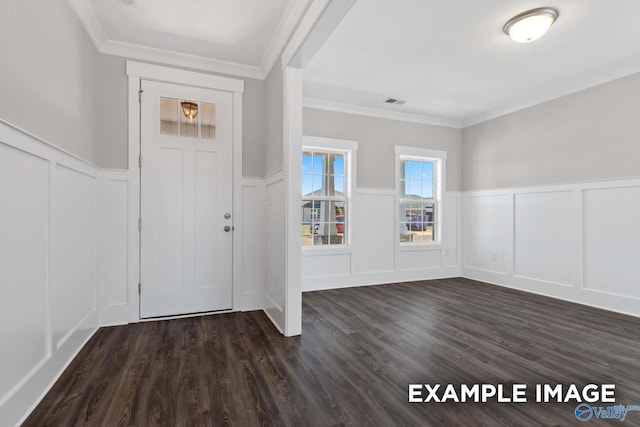 entrance foyer featuring crown molding, a decorative wall, dark wood-type flooring, and wainscoting