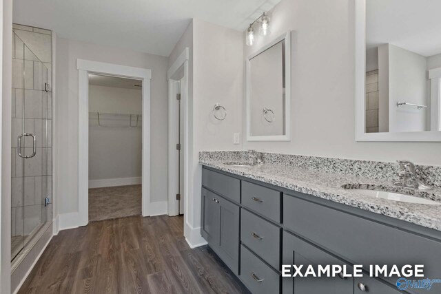 full bath featuring a walk in closet, a sink, a shower stall, and wood finished floors