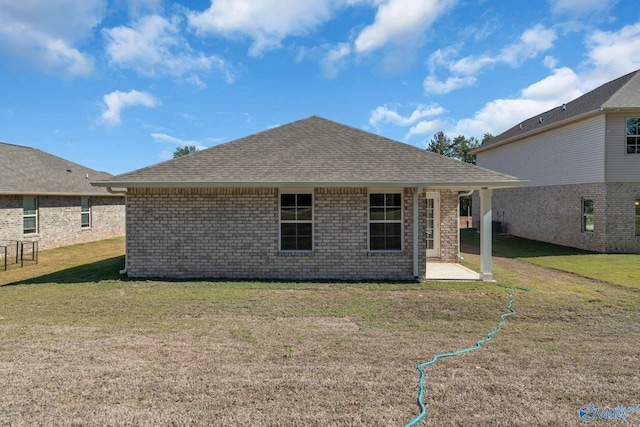 rear view of house with roof with shingles, brick siding, a patio area, and a lawn