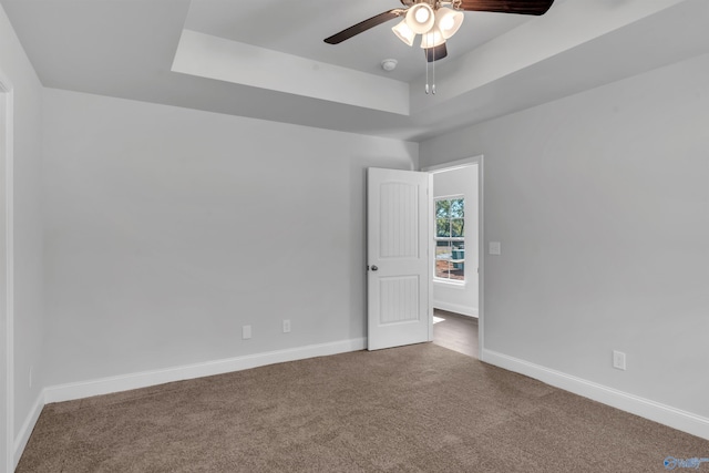 carpeted empty room featuring baseboards, a raised ceiling, and ceiling fan
