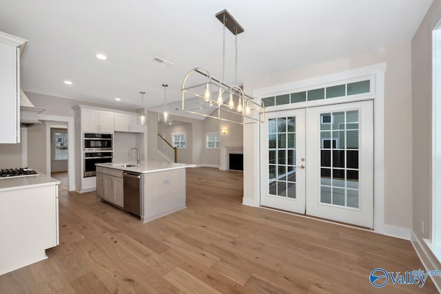 kitchen with a kitchen island with sink, a sink, open floor plan, light wood-style floors, and appliances with stainless steel finishes