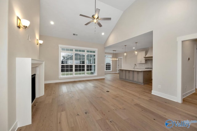 unfurnished living room with ceiling fan with notable chandelier, a fireplace, baseboards, and light wood-style floors