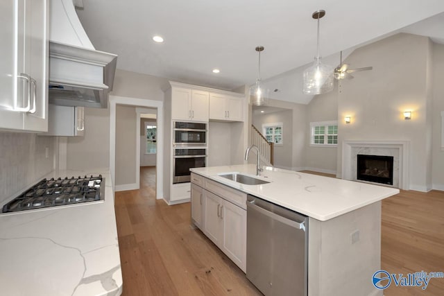 kitchen featuring custom range hood, a fireplace, stainless steel appliances, white cabinetry, and a sink