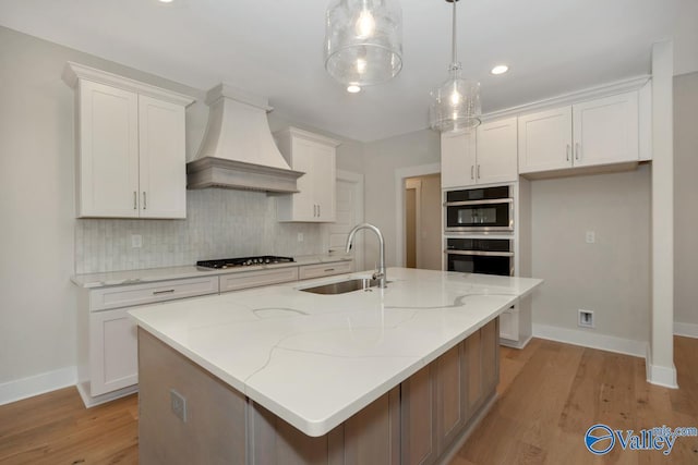 kitchen featuring premium range hood, a sink, gas cooktop, white cabinets, and decorative backsplash