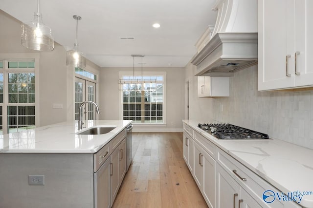 kitchen with light wood-type flooring, decorative backsplash, appliances with stainless steel finishes, custom exhaust hood, and a sink