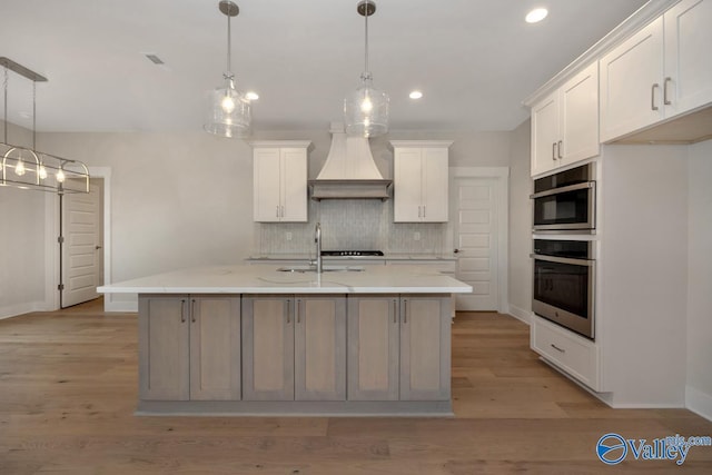 kitchen with tasteful backsplash, light wood-type flooring, stainless steel oven, custom exhaust hood, and white cabinetry