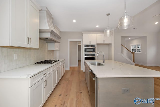 kitchen with light wood-style flooring, stainless steel appliances, decorative backsplash, a sink, and custom range hood