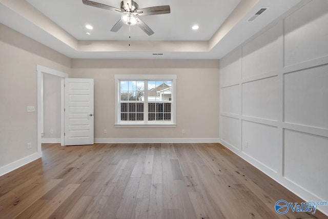 interior space featuring a raised ceiling, a decorative wall, visible vents, and light wood finished floors