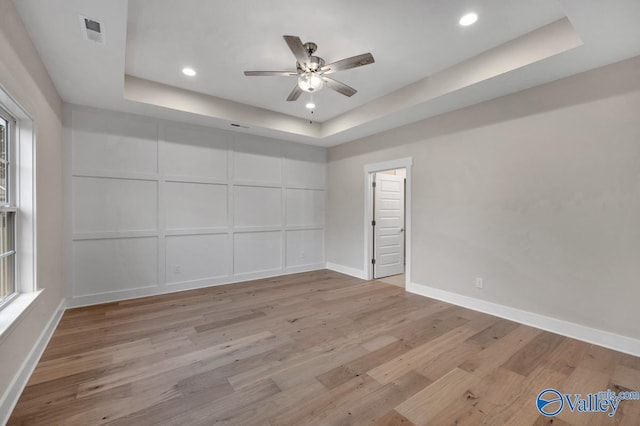 empty room with a ceiling fan, baseboards, visible vents, a tray ceiling, and light wood-type flooring