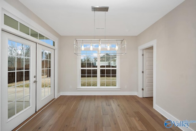 unfurnished dining area featuring wood finished floors, baseboards, and french doors