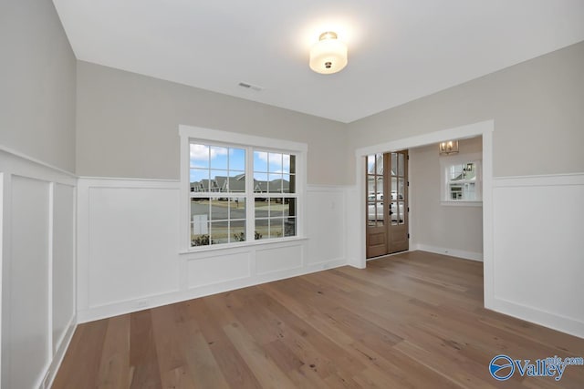 interior space with visible vents, wainscoting, a decorative wall, and wood finished floors