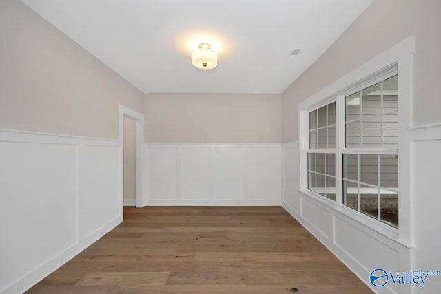 empty room with a wainscoted wall, wood finished floors, and a decorative wall