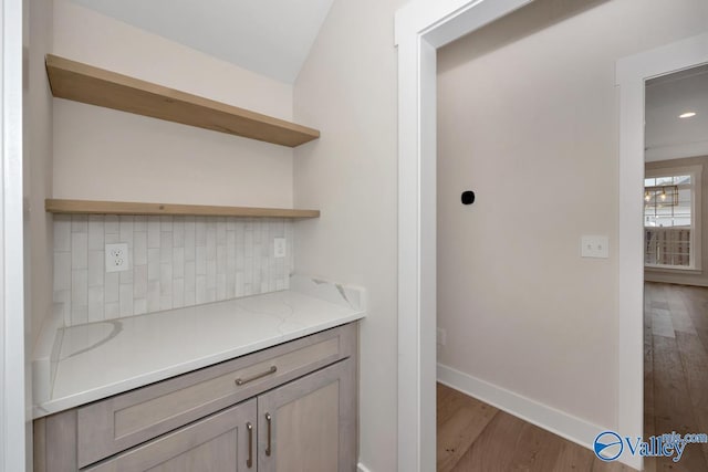 bar with wood finished floors, baseboards, and backsplash