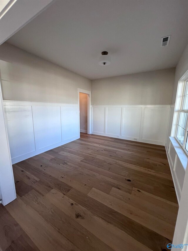 spare room featuring a wainscoted wall, a decorative wall, wood finished floors, and visible vents