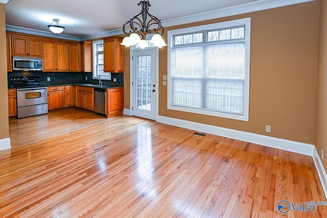 kitchen with tasteful backsplash, hanging light fixtures, light wood-type flooring, ornamental molding, and appliances with stainless steel finishes