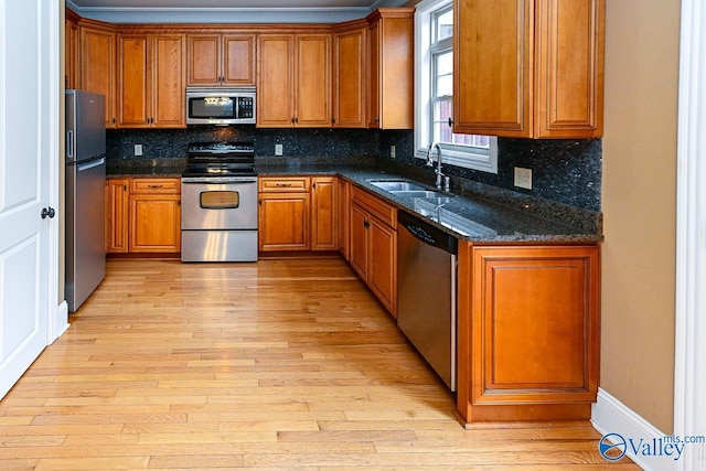 kitchen featuring dark stone countertops, sink, stainless steel appliances, and light wood-type flooring