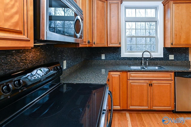 kitchen with sink, backsplash, stainless steel appliances, light hardwood / wood-style floors, and dark stone counters