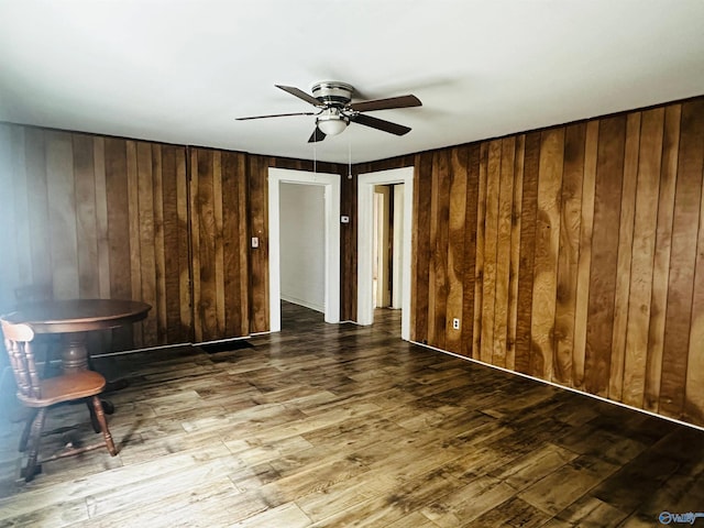 empty room featuring ceiling fan, wood walls, and hardwood / wood-style flooring