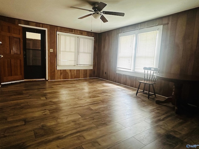 empty room with dark hardwood / wood-style floors, wood walls, and ceiling fan