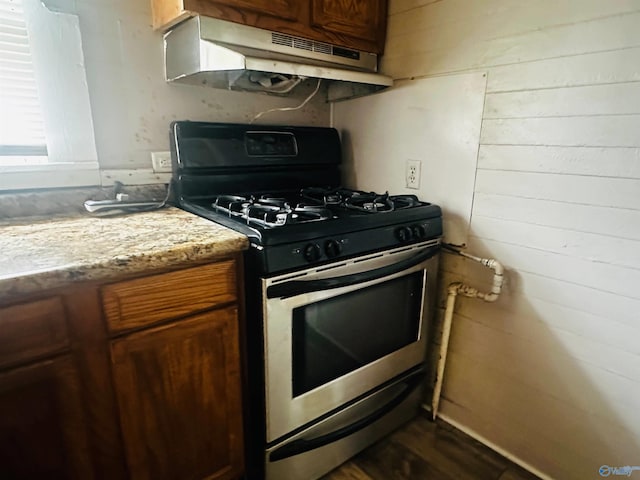 kitchen with hardwood / wood-style flooring, gas stove, and wood walls