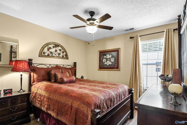 bedroom with a textured ceiling, ceiling fan, dark wood-type flooring, and visible vents