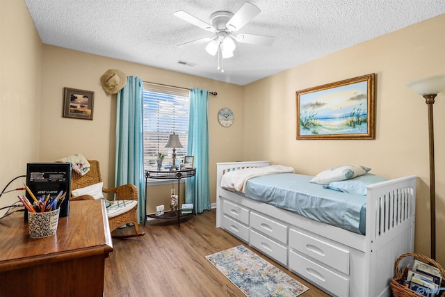 bedroom with ceiling fan, a textured ceiling, visible vents, and wood finished floors