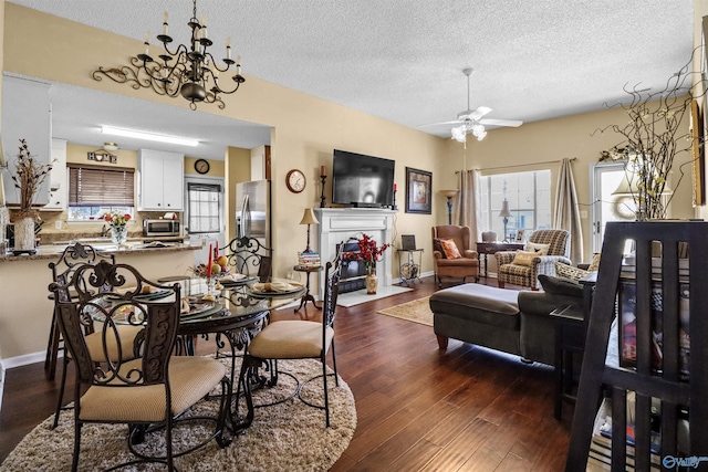 dining space with dark wood finished floors, a fireplace with flush hearth, a textured ceiling, baseboards, and ceiling fan with notable chandelier