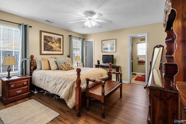 bedroom with a textured ceiling, wood finished floors, visible vents, and baseboards