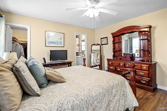 bedroom with a walk in closet, a ceiling fan, a textured ceiling, wood finished floors, and baseboards