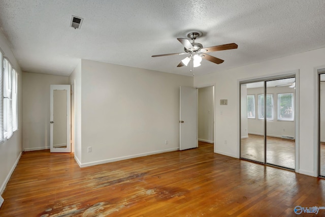 unfurnished bedroom with two closets, a textured ceiling, hardwood / wood-style floors, and ceiling fan