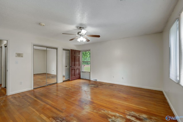 unfurnished bedroom featuring two closets, a textured ceiling, ceiling fan, and hardwood / wood-style floors