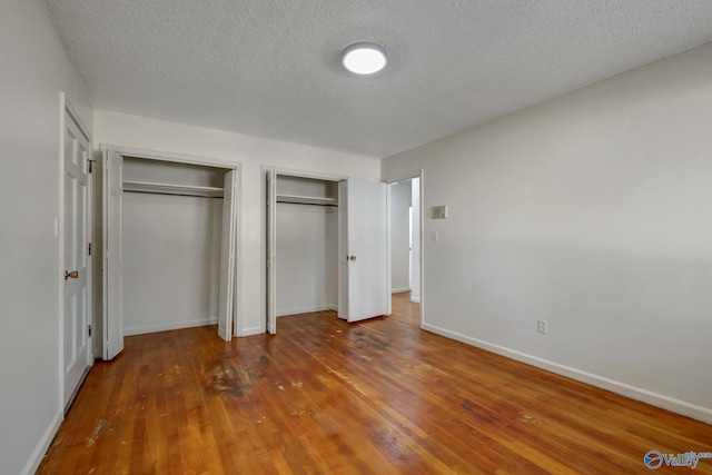 unfurnished bedroom with two closets, a textured ceiling, and hardwood / wood-style floors