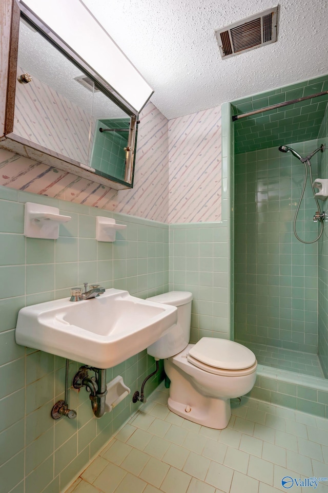 bathroom featuring tile walls, a tile shower, toilet, a textured ceiling, and tile patterned flooring