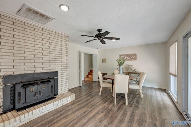 dining space with dark hardwood / wood-style floors, ceiling fan, a brick fireplace, and a textured ceiling