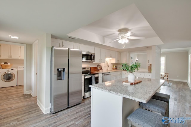 1908 Spanish Oaks Dr SE, Huntsville, AL 35803 - kitchen with appliances with stainless steel finishes, washing machine and dryer, a raised ceiling, light wood-style flooring, and a kitchen island